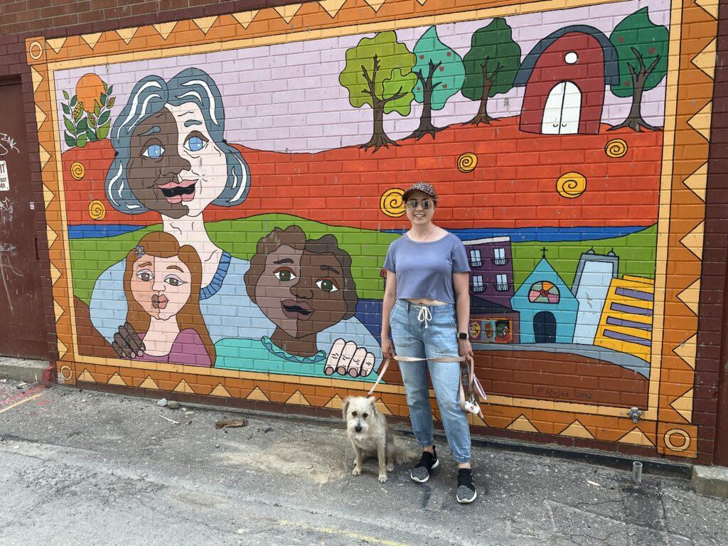woman and her small terrier dog standing in front of a bright mural in Downtown Kitchener
