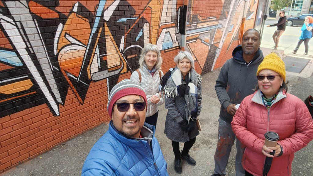 4 Stroll Walking Tour guests on the Cambridge Mural Tour where we met the artist Mediah painting a new mural in an alley. 