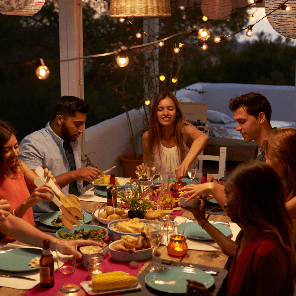 People seated around a dinner table with patio lighting and food on the table