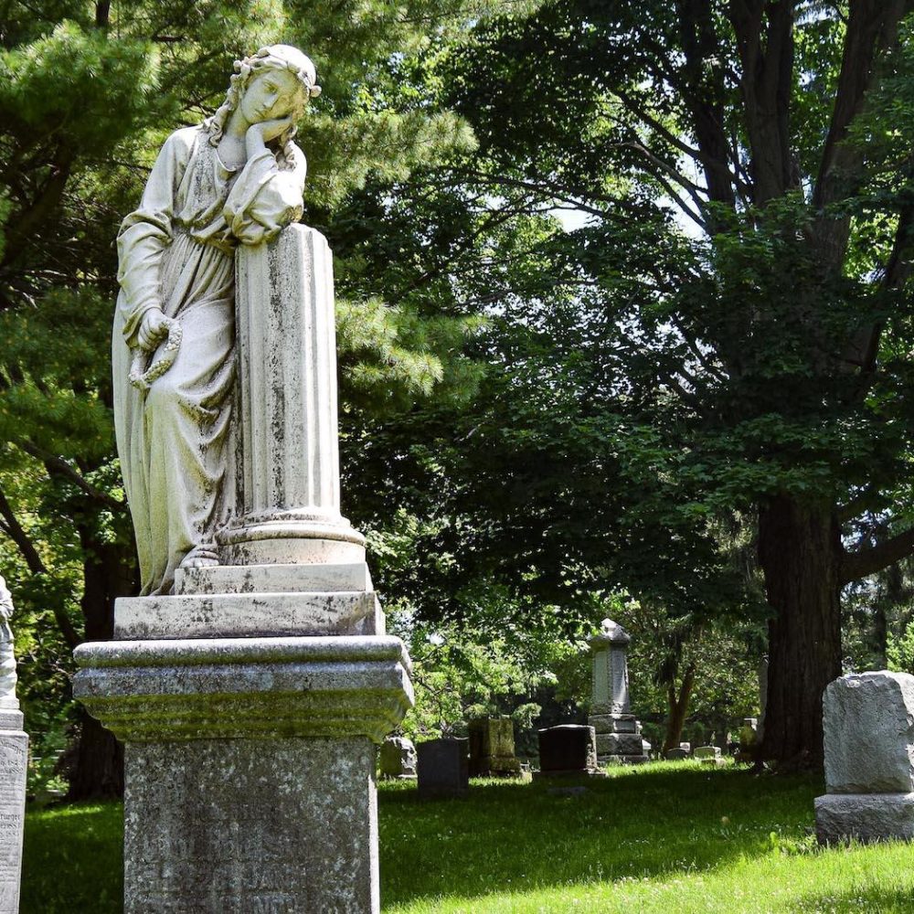 leaning statue against a green tree backdrop in Mount Hope Cemetery, Kitchener